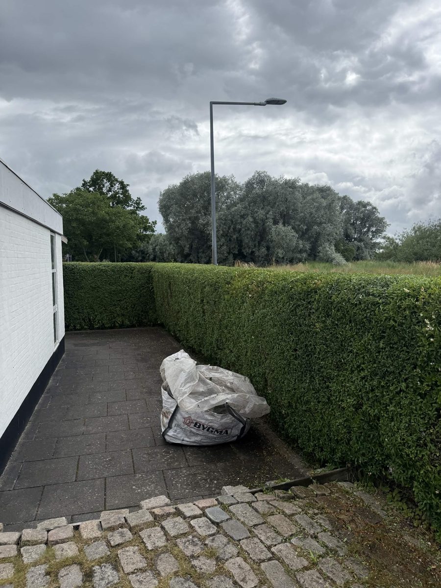 Afklip samlet i sæk ved siden af en nyklippet hæk, klar til bortkørsel
